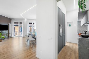 Eine moderne Küche mit Einbauofen, ein Essbereich mit Tisch und Stühlen und ein Blick ins Freie durch große Fenster.