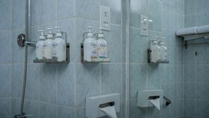 Un bagno con pareti piastrellate, una doccia e due ripiani con articoli da toilette.