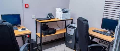 A small office with two desks, chairs, computers, and printers.