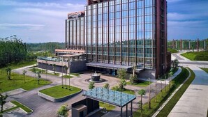 Um hotel moderno com fachada de vidro, nome em destaque no edifício e área de entrada ajardinada.