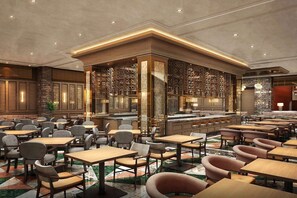 Un amplio vestíbulo de hotel con varias zonas de estar, un bar central y paneles decorativos en las paredes.