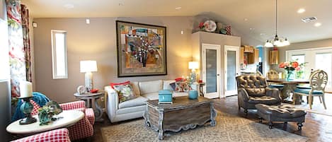 A living room with a sofa, armchairs, a coffee table, and a rug. There is a dining area with a table and chairs.
