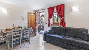 Un coin repas avec une table dressée pour deux personnes, un canapé et une vue sur un balcon.