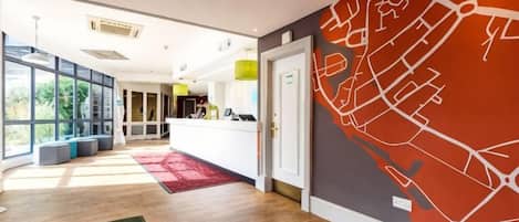 Un moderno vestíbulo de hotel con un mostrador de recepción, un amplio muro con ventanas y un mural de un mapa rojo.