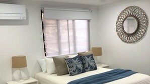 A bedroom with a bed, two bedside tables, a ceiling fan, a window with blinds, and a wall-mounted mirror. - Archer View - 72 Archer Steet, Emu Park (Emu Park)