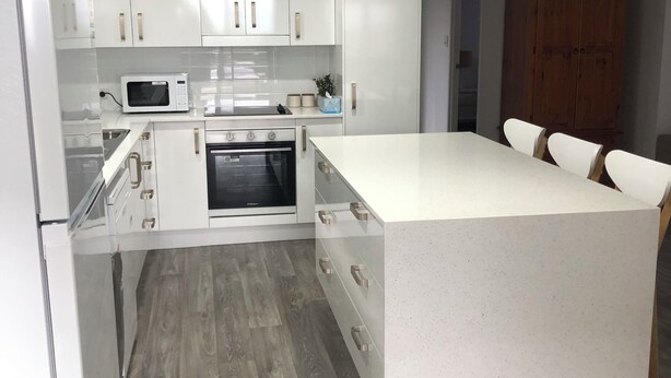 A modern kitchen with white cabinets, a central island, and a wooden floor. - Archer View - 72 Archer Steet, Emu Park (Emu Park)
