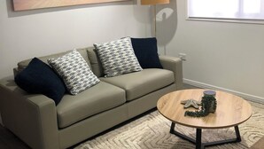 A living room with a beige sofa, patterned cushions, a round coffee table with a starfish decoration, a lamp, and a painting of a beach scene. - Archer View - 72 Archer Steet, Emu Park (Emu Park)