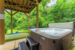 A hot tub under a wooden pergola with a grassy area and trees in the background.