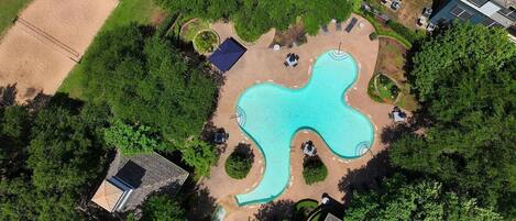 An aerial view of a swimming pool with a unique shape, surrounded by greenery and a few seating areas.