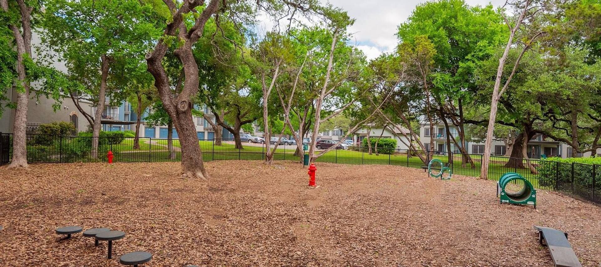 Un parque con árboles, un área de juegos y un hidrante rojo.