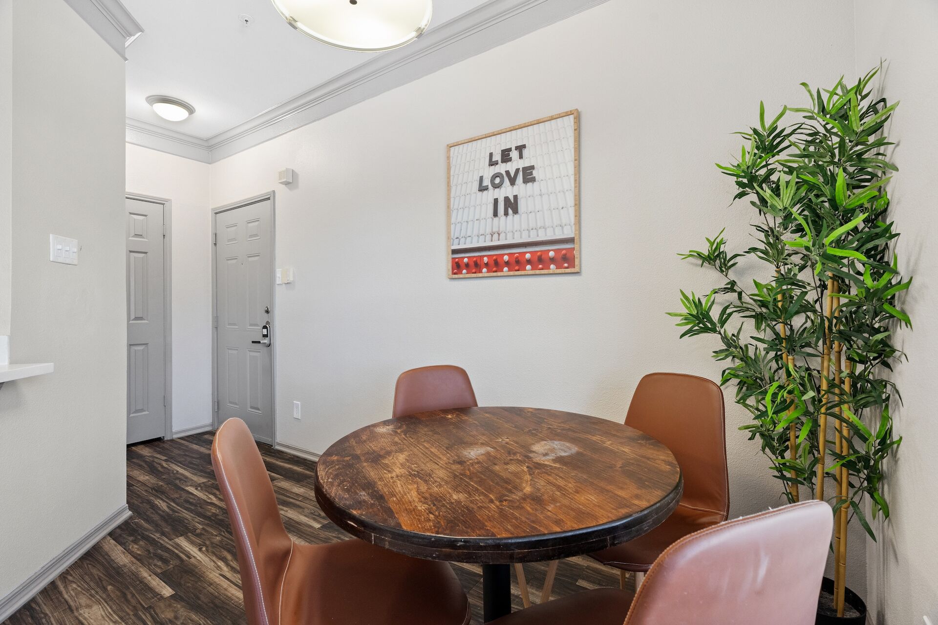 A conference room with a wooden table and leather chairs, a 'LET LOVE IN' sign on the wall, and a bamboo plant.