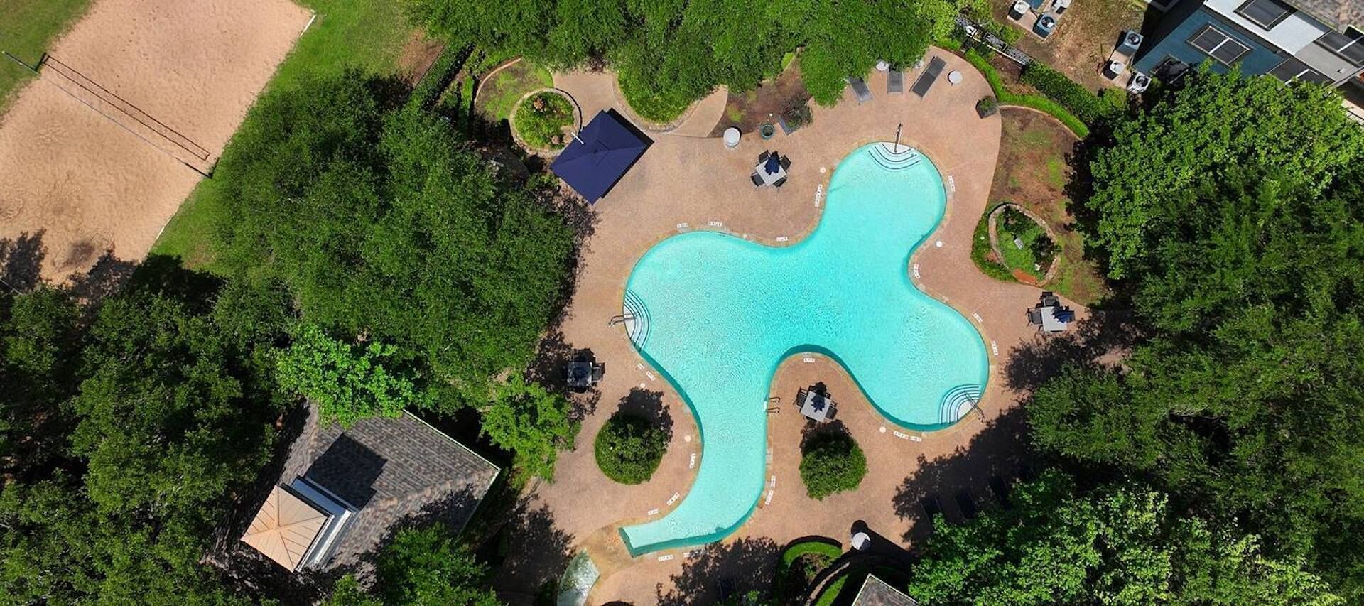 An aerial view of a swimming pool with a unique shape, surrounded by greenery and a few seating areas.