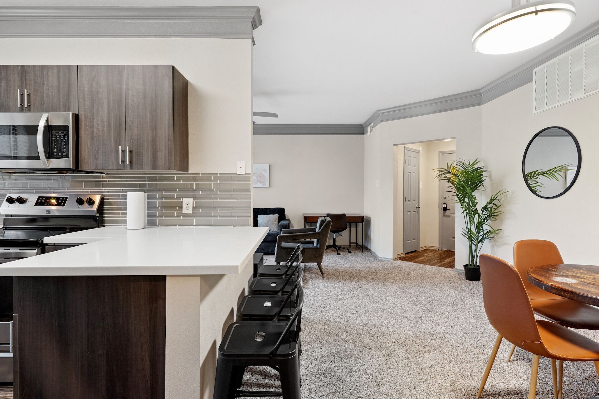 A modern kitchen with a central island, a dining area with a round table and chairs, and a hallway leading to another room.