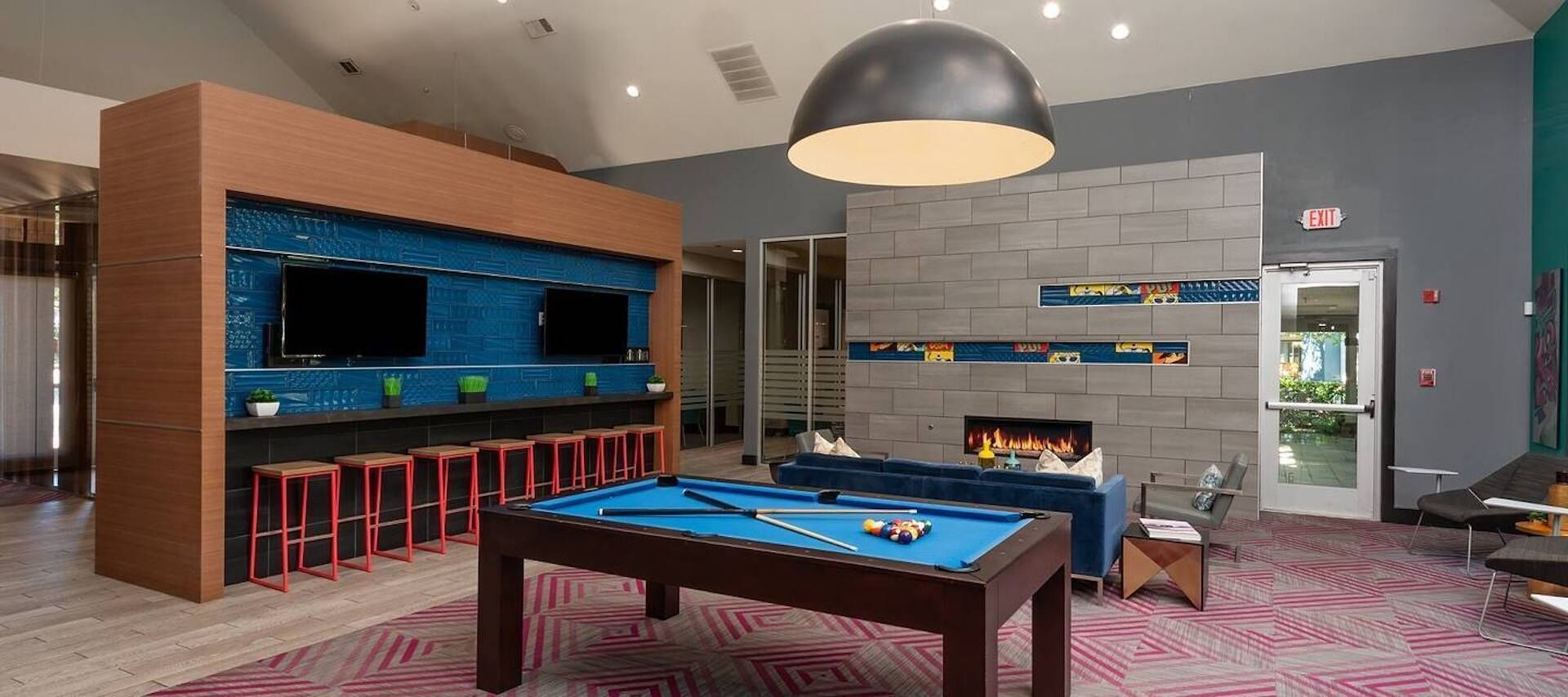 A pool table in a modern lounge area with a fireplace and a bar.