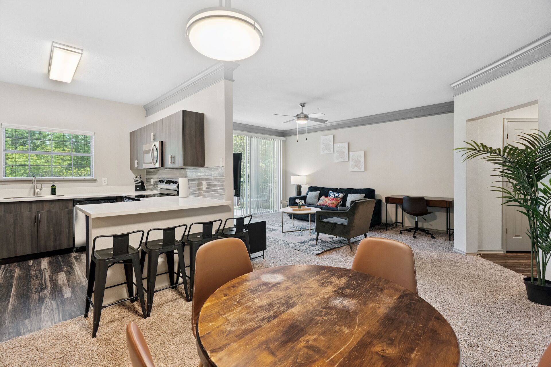 A modern kitchen with a central island, dining area with a round wooden table, and a living room with a sofa and chairs.