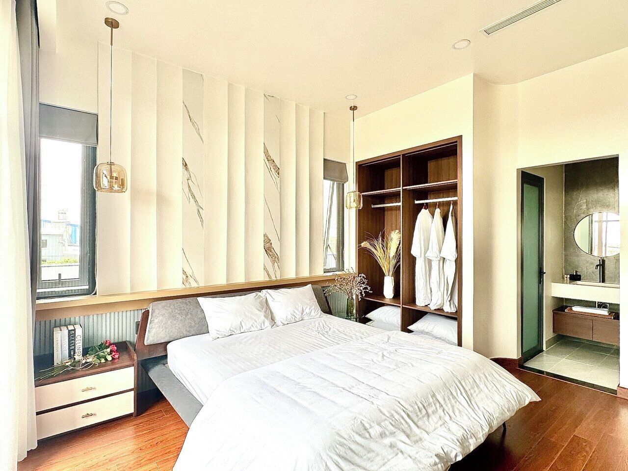 A modern bedroom with a large bed, a walk-in closet, a bathroom with a mirror, and a window with curtains.