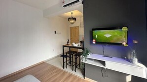 Egy modern nappali, melyben egy síkképernyős televízió van felszerelve egy sötét színű falra, egy fa étkezőasztal székekkel, és egy kis, fehér konzolasztal, melyen egy váza áll.