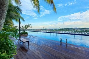 Eine Holzterrasse mit Pool, Palmen und Blick auf eine Stadtlandschaft.