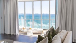 Ein modernes Hotelzimmer mit großem Fenster zum Meer, einem weißen Sofa und einem kleinen Tisch mit Blumenvase.