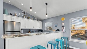 Une cuisine moderne avec des meubles blancs, un réfrigérateur en acier inoxydable, un comptoir en granit et un coin bar agrémenté de tabourets turquoise.