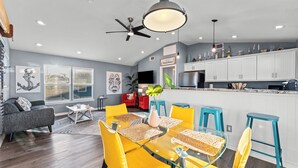 Une cuisine moderne avec des meubles blancs, un îlot central et un coin repas agrémenté de chaises jaunes et d’une table en verre.