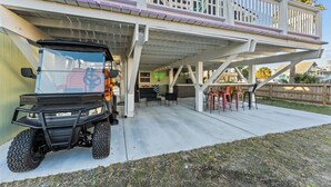 Une voiturette de golf est garée sous une terrasse couverte, avec des sièges d’extérieur et une pancarte indiquant « Bienvenue ».