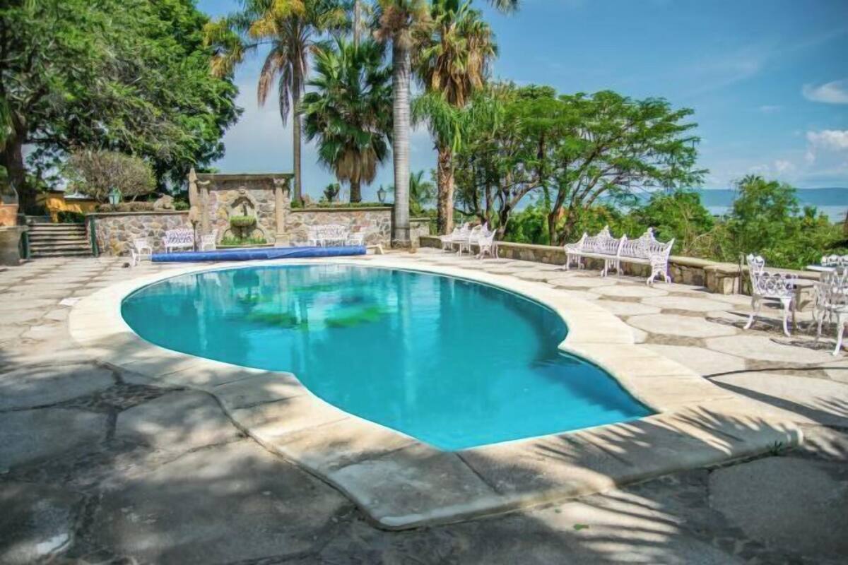 Ein Pool mit gewölbter Kante, umgeben von Steinplatten und weißen Stühlen.