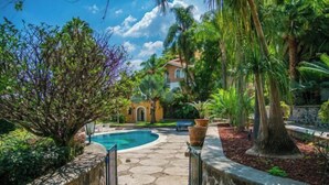 A pool area with a stone pathway, surrounded by tropical plants and a building with a red roof. - ANANA Rancho San Rafael Pool and Lake Views (Ajijic)