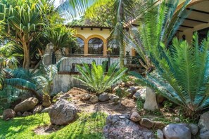 A garden with tropical plants, rocks, and a building with arched windows. - ANANA Rancho San Rafael Pool and Lake Views (Ajijic)
