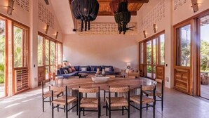 A spacious room with a round wooden dining table, wicker chairs, a blue sofa, and large windows allowing natural light. - ANANA Casa Kaab Kaan Rooftop pool & Beachfront (Tulum)
