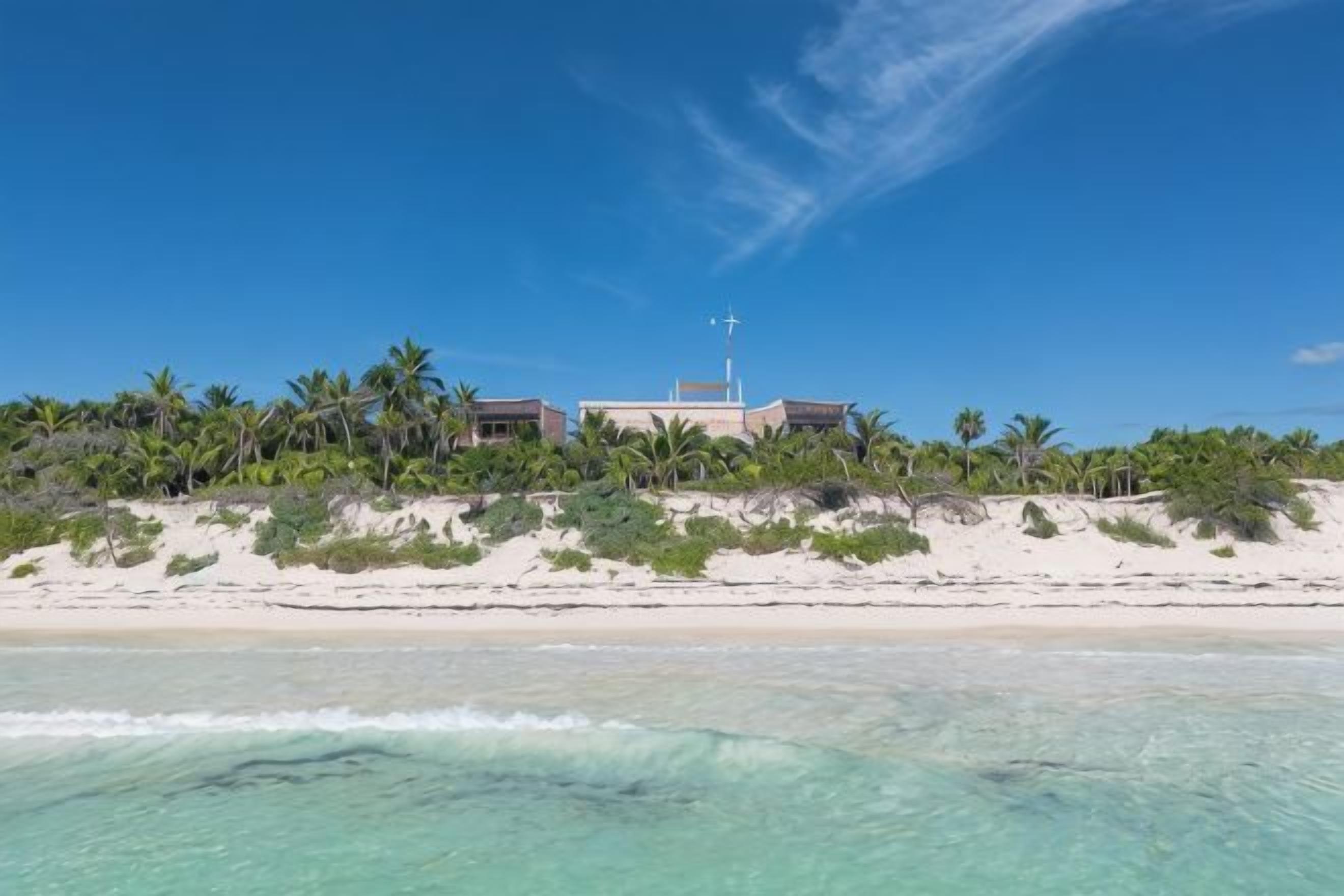 A beachfront property with a large building, sandy beach, and palm trees.