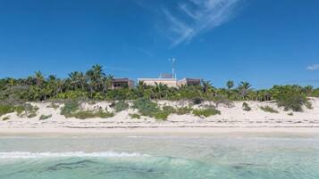 A beachfront property with a large building, sandy beach, and palm trees.