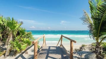 A wooden pathway leading to a beach with clear turquoise water and palm trees.