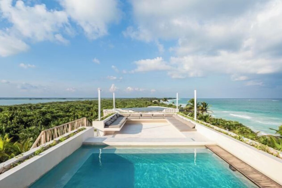 A pool area with a view of the ocean, surrounded by lush greenery.