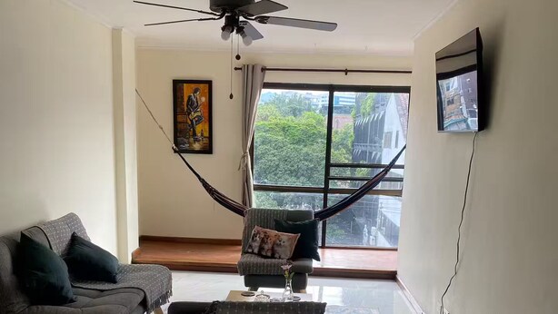 A living room with a hammock, two sofas, a television, and a large window with a view of trees and buildings. - Comfortable and safe apartment with river view (Medellín)