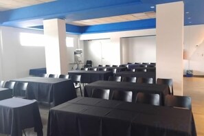 A conference room with rows of tables and chairs, a coffee machine, and a large window. - Ibis Budget Aguascalientes (Aguascalientes)