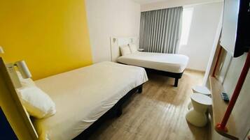 Habitación de hotel con dos camas, una mesita redonda, un inodoro y una ventana con cortinas.