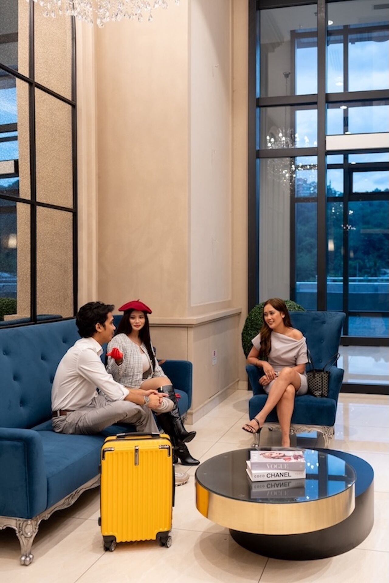 Eine moderne Lobby mit einem blauen Sofa, einem gelben Koffer und einem runden Couchtisch mit Büchern.