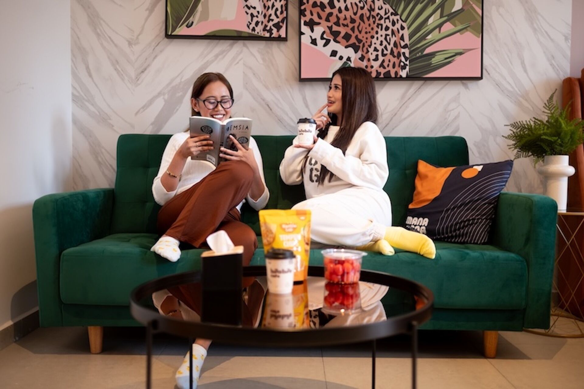 Twee personen zitten op een groene bank met een bijzettafeltje ervoor.