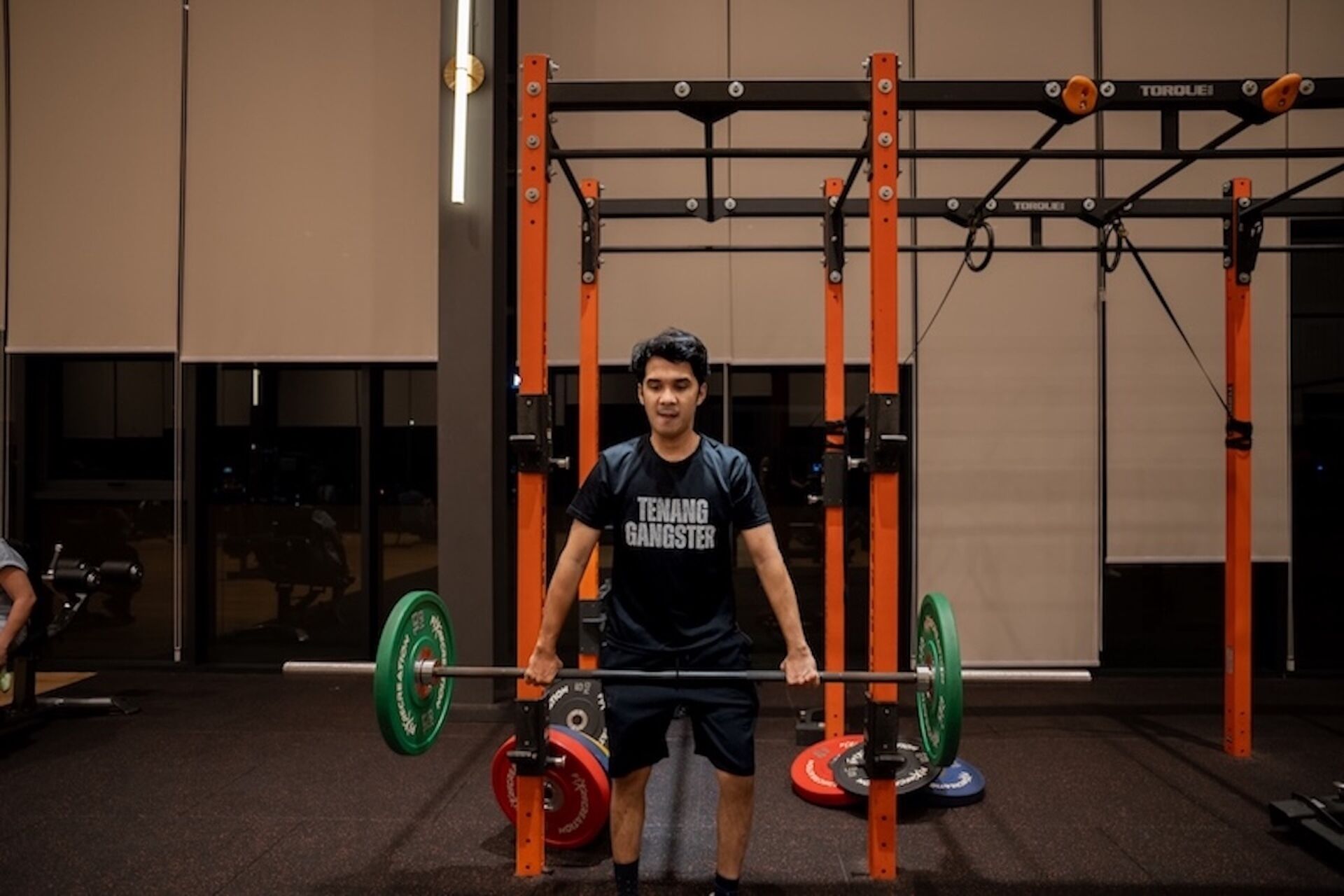A person lifting a barbell in a gym with weightlifting equipment and a squat rack.
