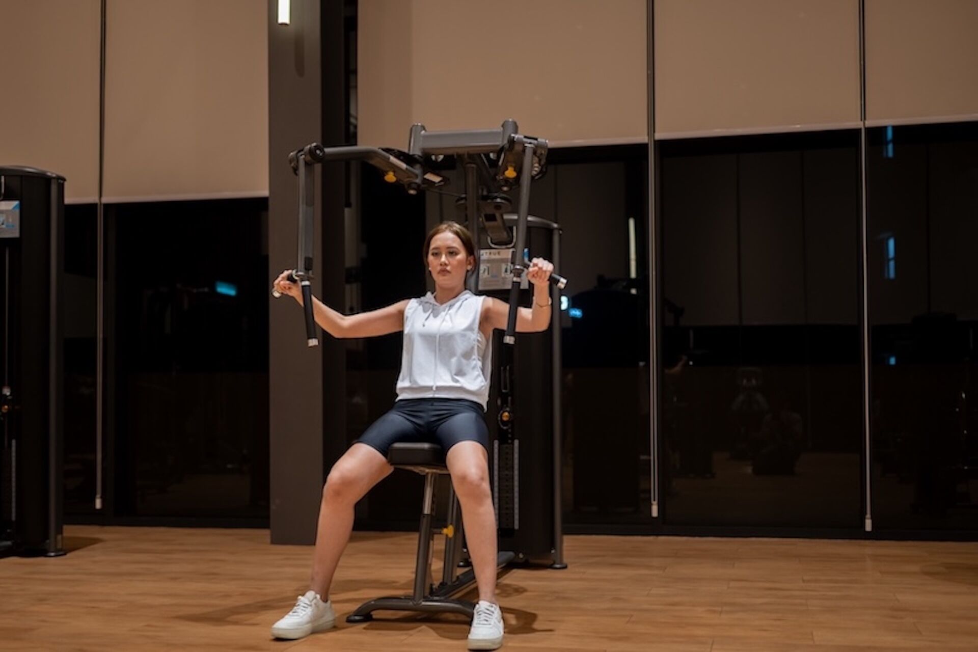 Una persona ejercitando en una máquina en un gimnasio con suelo de madera y ventanas amplias.