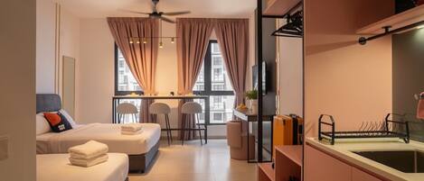 A modern hotel room with two beds, a dining area, a kitchenette, and a large window with curtains.