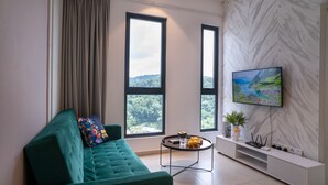 A modern living room with a teal sofa, a round coffee table, and a TV mounted on a marble-patterned wall. - Paxtonz KL Walk to Mall & Pool (Petaling Jaya)