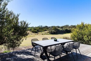 Une terrasse extérieure en bois, avec une table et des chaises, entourée de verdure et offrant une vue dégagée sur un paysage vallonné.
