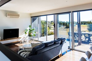 A modern living room with a large TV, a sofa, and a dining area with outdoor seating. - St Andrews Golf Course & Nature Getaway (Fingal)