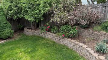 A landscaped backyard with a stone retaining wall, a variety of shrubs, and a well-maintained lawn.