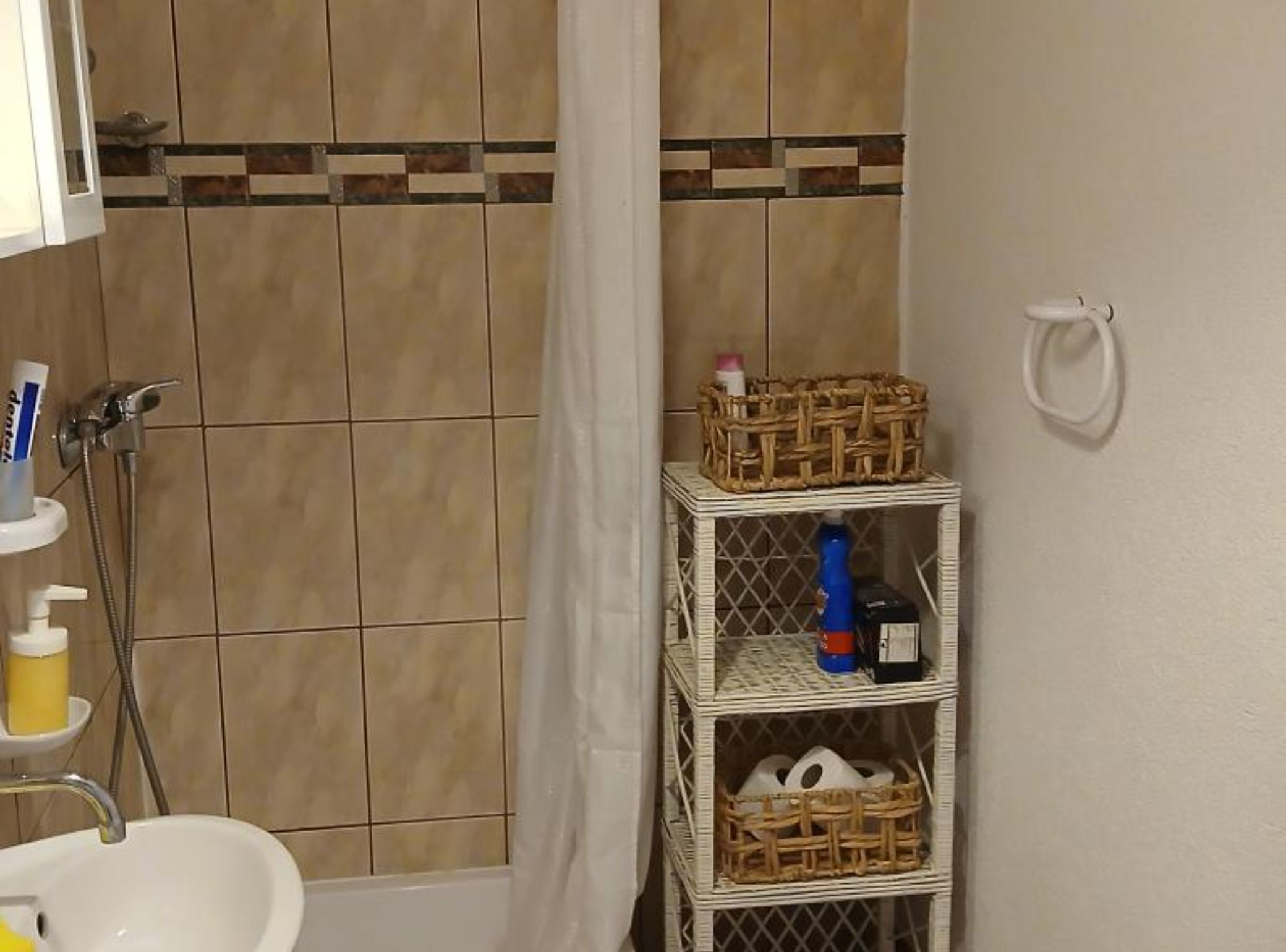 A bathroom with a shower, a sink, and a small shelf with toiletries.