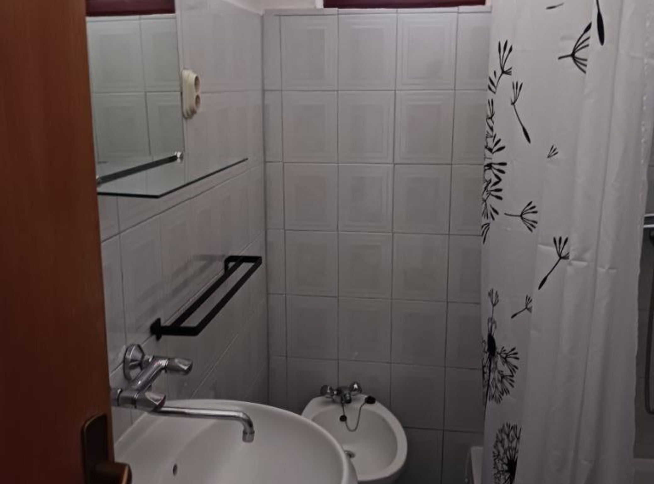 Ein Badezimmer mit einem weißen Waschbecken, einem Spiegel und einer Duschvorhang mit floralem Muster.