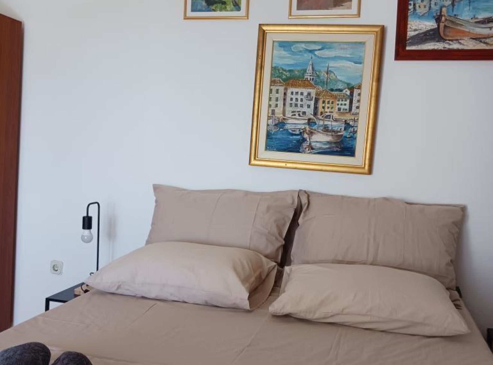 A bedroom with a bed, two pillows, a nightstand, and a wall-mounted lamp.
