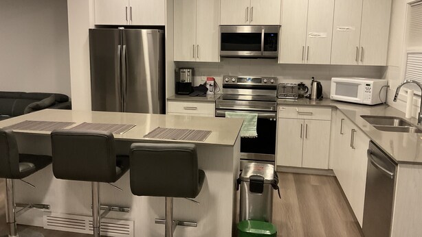 A modern kitchen with stainless steel appliances, a central island with bar stools, and a green trash bin.